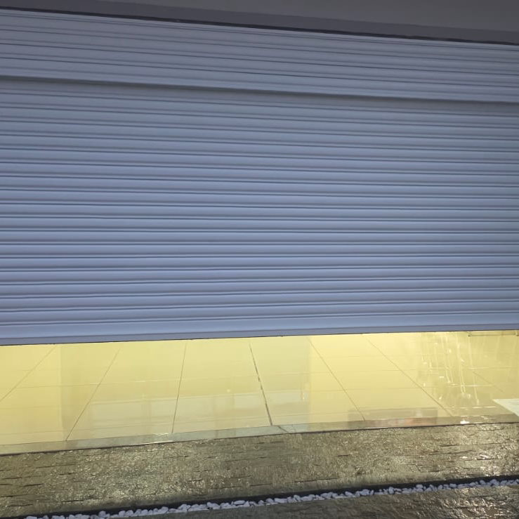 Portão de enrolar branco meio aberto, com a garagem iluminada atrás