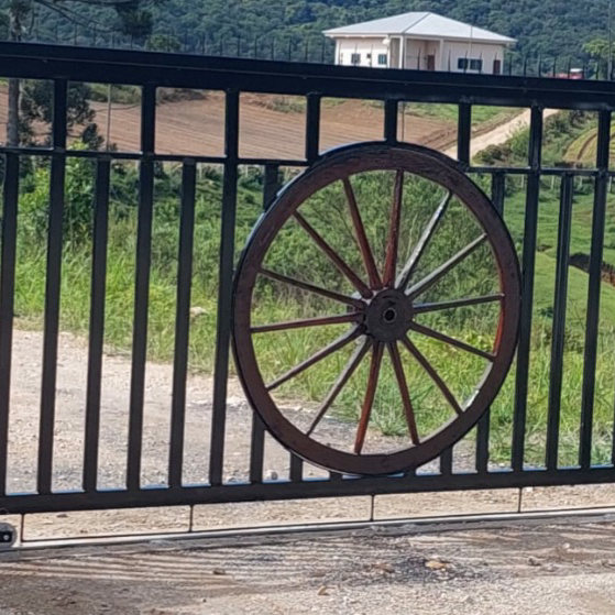 Portão de correr preto com uma roda de carroça de madeira no meio